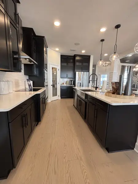 A sleek, modern kitchen with white cabinetry, stainless steel appliances, and pendant lighting in Eden at Crossprairie by M/I Homes (St. Cloud, FL).