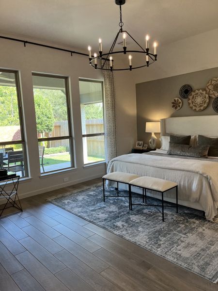 A serene bedroom with elegant chandelier, neutral decor, large windows, and a cozy seating area. A serene bedroom with elegant chandelier, neutral decor, large windows, and a cozy seating area.