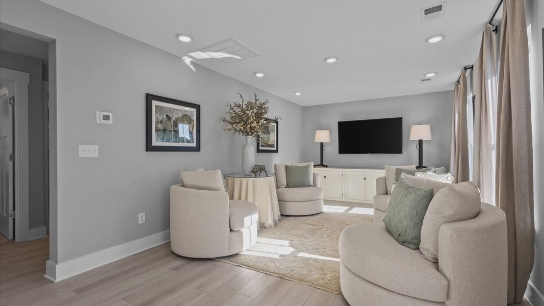 Loft space with large windows, gray walls, and hardwood flooring with tall ceilings at Pleasant Falls by DRB Homes