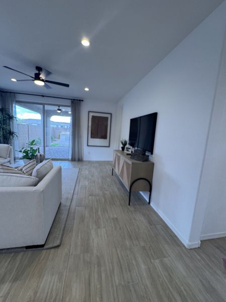 A modern living room with sleek wood floors, a ceiling fan, and sliding glass doors opening to a patio.