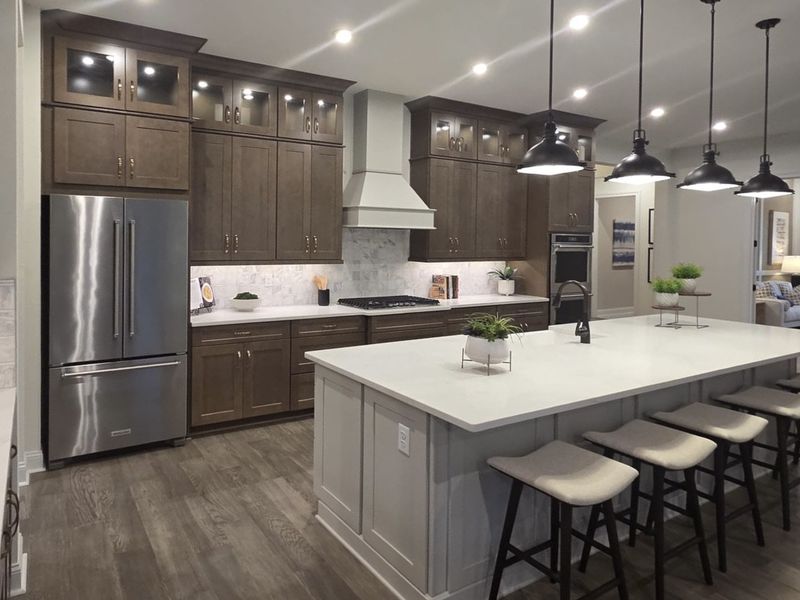A modern kitchen featuring dark wood cabinets, stainless steel appliances, and a spacious island with pendant lighting.