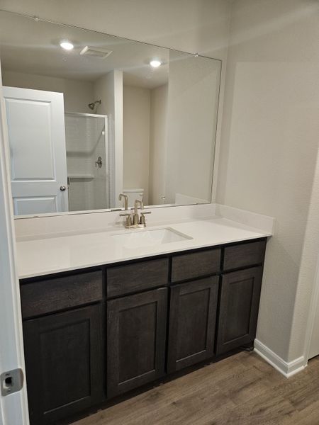 A modern bathroom features a sleek countertop, large mirror, dark wood vanity, and bright lighting.