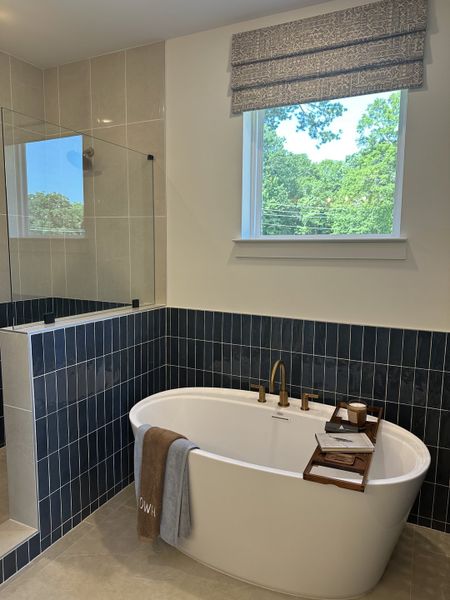 A serene bathroom featuring a white freestanding tub, sleek dark tiles, and a large window with nature views.