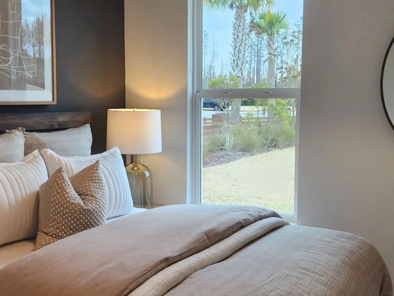 A cozy bedroom featuring soft, textured bedding, a modern lamp, and a scenic window view with palm trees outside.