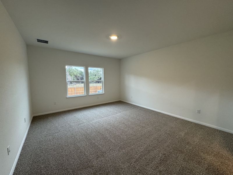 A spacious, carpeted room with neutral walls, ceiling light, and large windows for natural light. Ideal for versatile use.