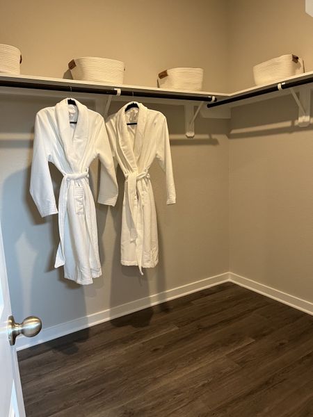 A spacious walk-in closet with sleek wooden floors, white robes, and woven storage baskets on shelves.