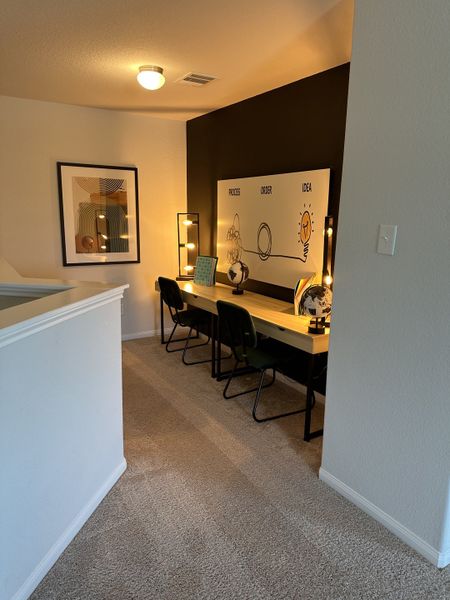 A cozy workspace with dual desks, modern art, and warm lighting on soft carpet flooring.