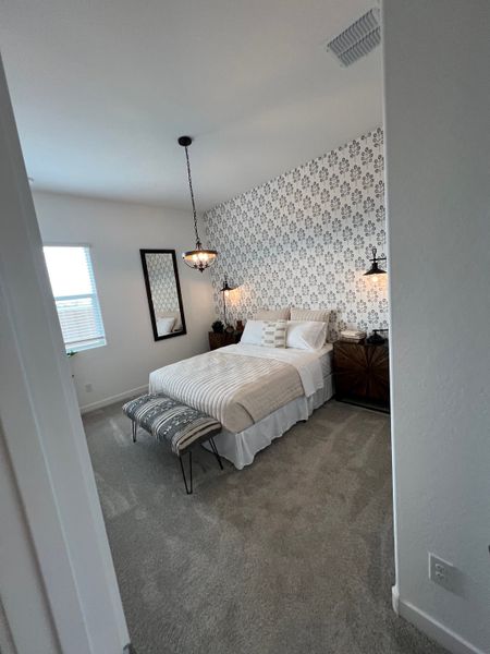 A cozy bedroom with patterned wallpaper, a plush bed, elegant lighting, and a bench at its foot.