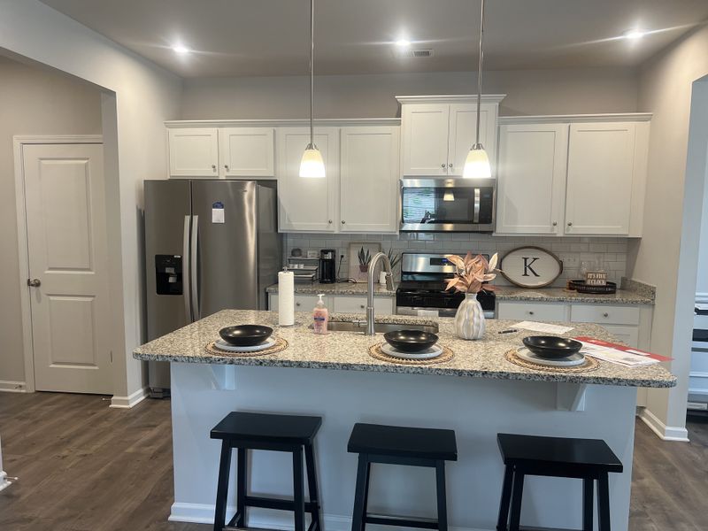 A modern kitchen with granite countertops, sleek stainless steel appliances, and elegant pendant lights, featuring a cozy island seating area. A modern kitchen with granite countertops, sleek stainless steel appliances, and elegant pendant lights, featuring a cozy island seating area.