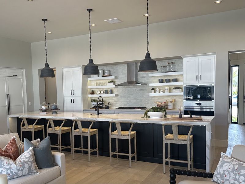 A modern kitchen with open shelving, sleek black pendant lights, and a spacious island with bar seating.
