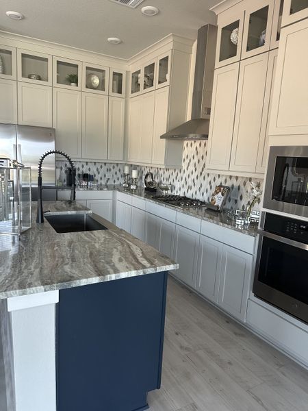 A modern kitchen with sleek white cabinets, patterned backsplash, and a navy island featuring a marble countertop.