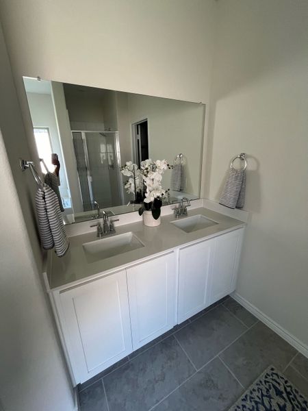 A modern bathroom featuring dual sinks, a large mirror, elegant tile flooring, and tasteful floral decor.