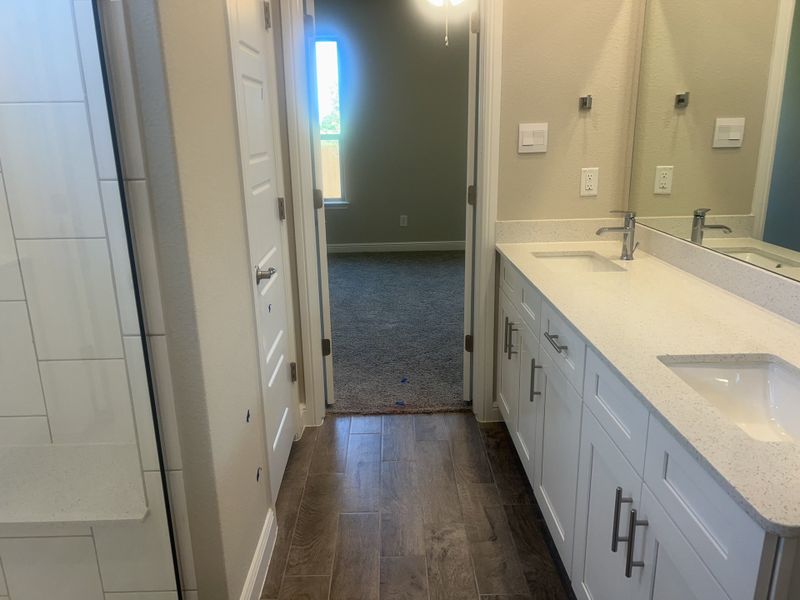 A modern bathroom featuring dual sinks, sleek white cabinetry, and a spacious shower with elegant wood-look flooring. A modern bathroom featuring dual sinks, sleek white cabinetry, and a spacious shower with elegant wood-look flooring.
