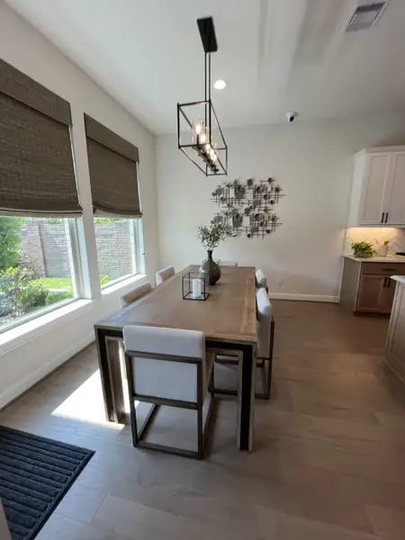A modern dining area with natural light, featuring a wooden table, elegant chairs, and contemporary lighting.