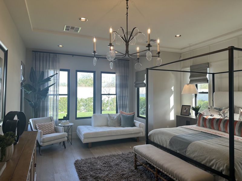 A cozy bedroom with a canopy bed, elegant chandelier, large windows, and plush seating, creating a serene retreat.