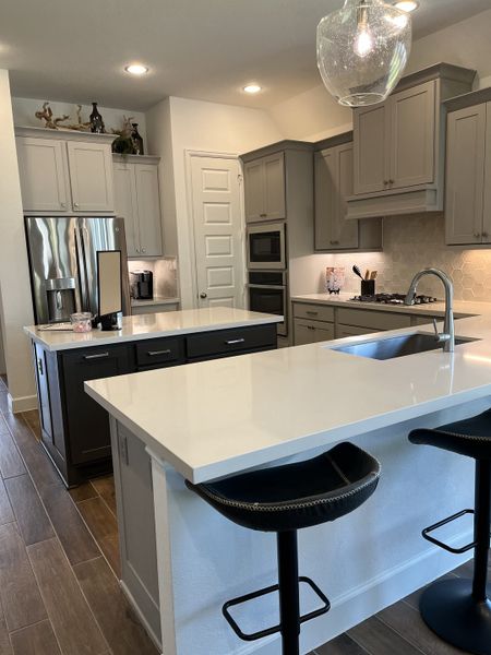 A modern kitchen featuring sleek gray cabinets, a spacious island with white countertops, and elegant pendant lighting.