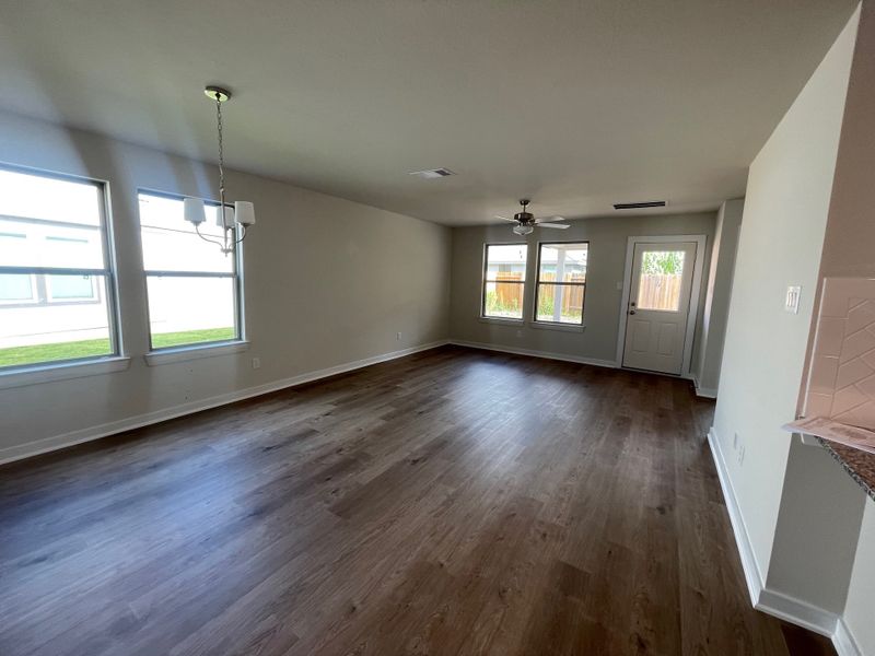 A spacious living area with large windows, warm wood flooring, and modern chandelier in a neutral palette.
