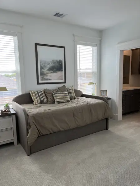A cozy bedroom with a daybed, striped pillows, and soothing artwork, featuring soft carpet and natural light.