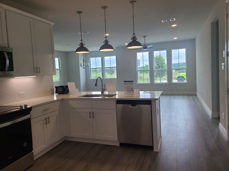A modern kitchen with white cabinetry, stainless steel appliances, pendant lighting, and large windows overlooking greenery. A modern kitchen with white cabinetry, stainless steel appliances, pendant lighting, and large windows overlooking greenery.