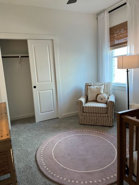 A cozy nursery with a striped armchair, soft pink rug, and gentle lighting.