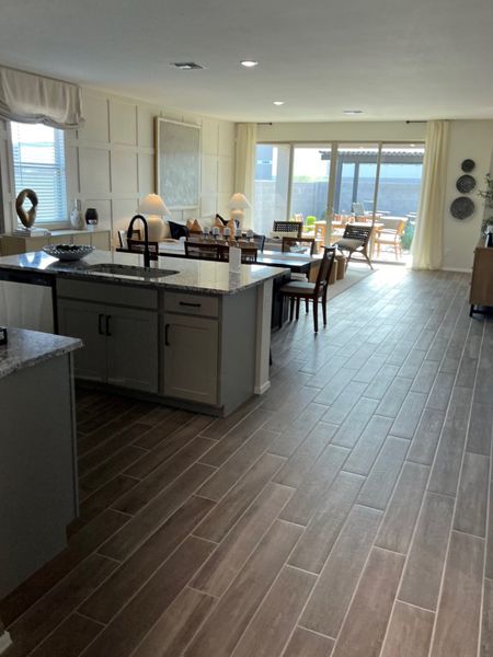 An open-concept living area featuring wood-look tile, modern kitchen, and sunlit dining leading to a spacious patio.