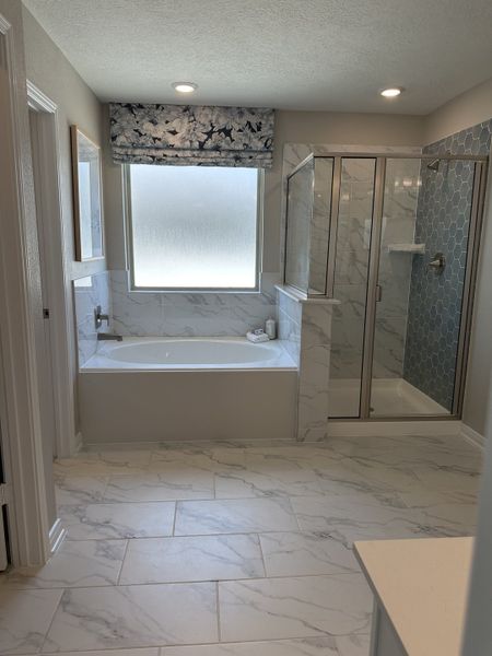 A modern bathroom featuring a marble-tiled bathtub, sleek shower, and patterned window treatment for a touch of elegance.