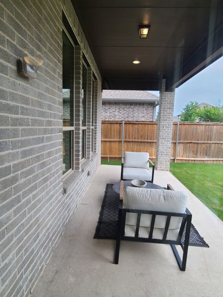 A cozy covered patio with modern chairs and a rug, perfect for relaxation and enjoying the outdoors.