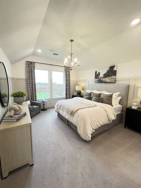 A cozy bedroom with a plush bed, elegant chandelier, and natural light streaming through large windows.
