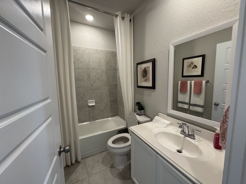 A sleek bathroom with gray tile, white vanity, and elegant decor, featuring framed art and plush towels for a cozy feel. A sleek bathroom with gray tile, white vanity, and elegant decor, featuring framed art and plush towels for a cozy feel.