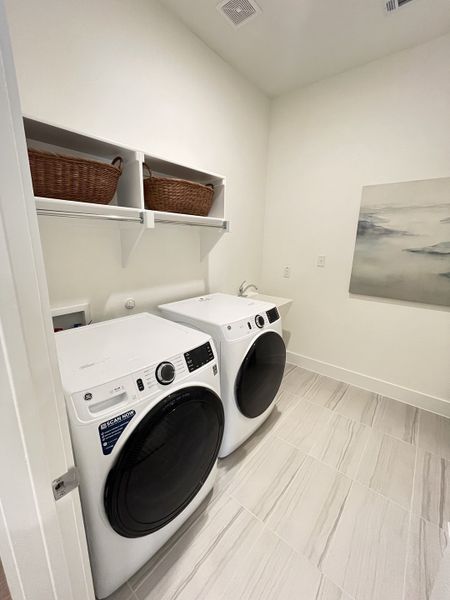 A modern laundry room with sleek white appliances, open shelving, and elegant tile flooring. A modern laundry room with sleek white appliances, open shelving, and elegant tile flooring.