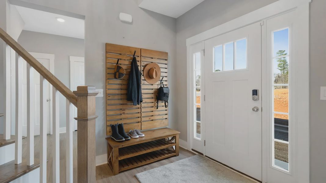 Entry with two story ceiling, oak stairs, open railing, mudroom, and LVP flooring at Village at Midway by DRB Homes Entry with two story ceiling, oak stairs, open railing, mudroom, and LVP flooring at Village at Midway by DRB Homes