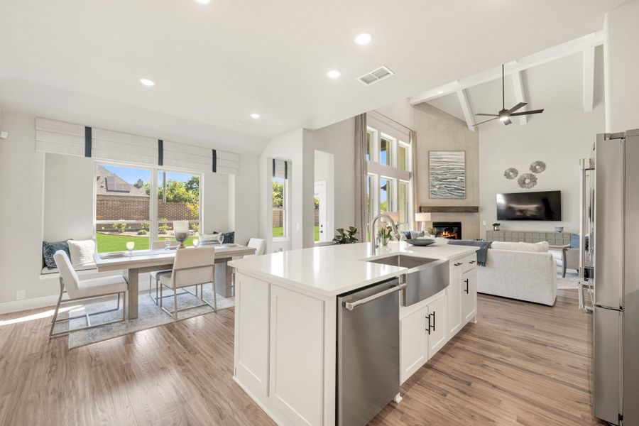 Open-concept kitchen with white island, stainless appliances, and hardwood floors flowing into dining and living areas with vaulted ceiling