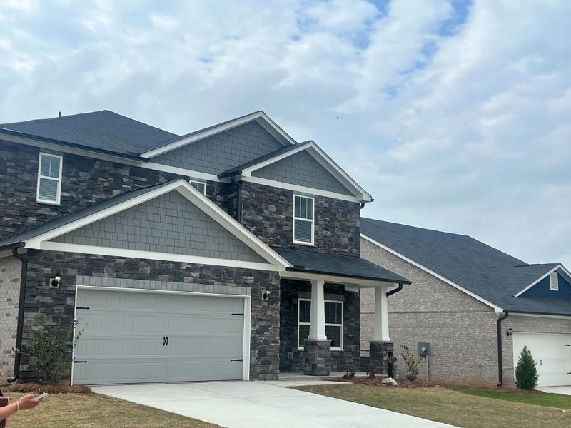 A charming grey stone home with a spacious driveway in Creekside at Oxford Park by Meritage Homes (Fairburn, GA).