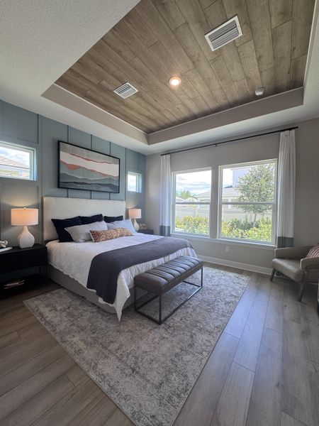 A serene bedroom with a tray ceiling, large windows, and elegant decor featuring a plush bed and cozy lighting.