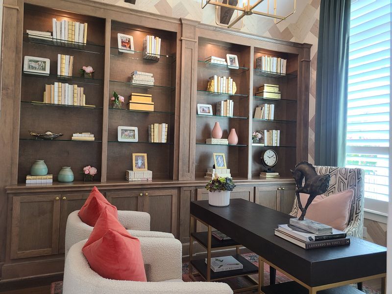 A cozy library with dark wood built-ins, plush seating, coral accents, and elegant decor under warm lighting. A cozy library with dark wood built-ins, plush seating, coral accents, and elegant decor under warm lighting.