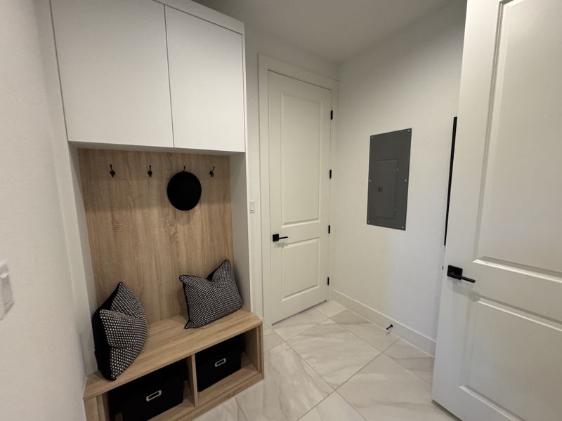 A modern mudroom with sleek storage cabinets, a wooden bench, decorative pillows, and marble-tiled flooring.