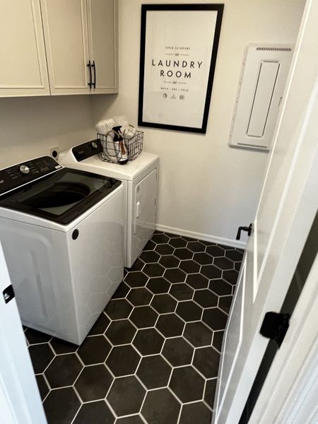 A small but efficient laundry room with cabinetry, stylish decor, and a bold black-and-white tile pattern.