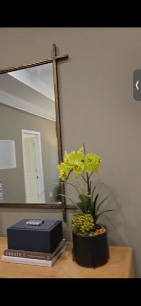 A sophisticated interior space featuring a decorative mirror, potted orchid, and stacked books on a wooden console.