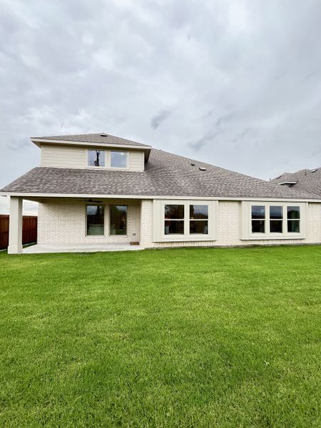 A modern beige brick home with abundant windows and a lush lawn in Stone River Glen 60s by Bloomfield Homes (Royse City, TX).