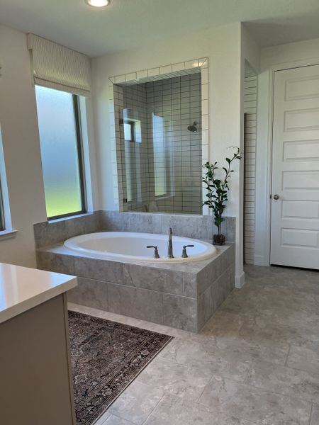 A modern bathroom featuring a luxurious soaking tub, tile flooring, and a sleek shower with natural light.