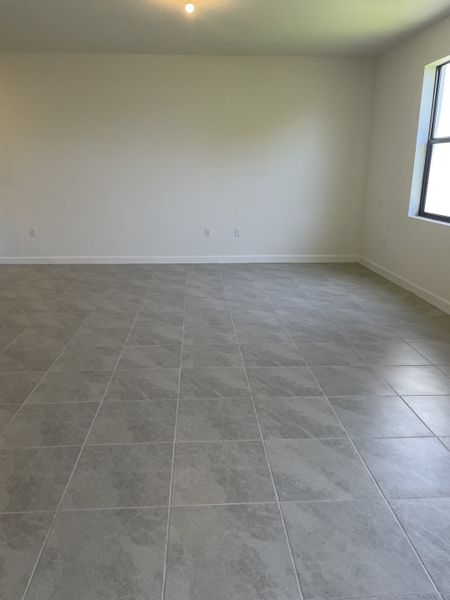 A spacious room with sleek grey tiled floors and neutral walls, offering abundant natural light from a large window.