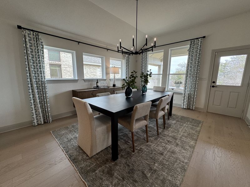 A modern dining room with a sleek black table, elegant chairs, and large windows offering natural light.