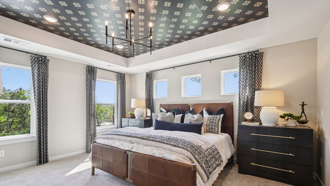 Large primary bedroom with accent tray ceiling and multiple windows for natural light