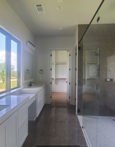 A spacious, elegant bathroom featuring dual sinks, a large window, and a glass-enclosed shower with sleek finishes.