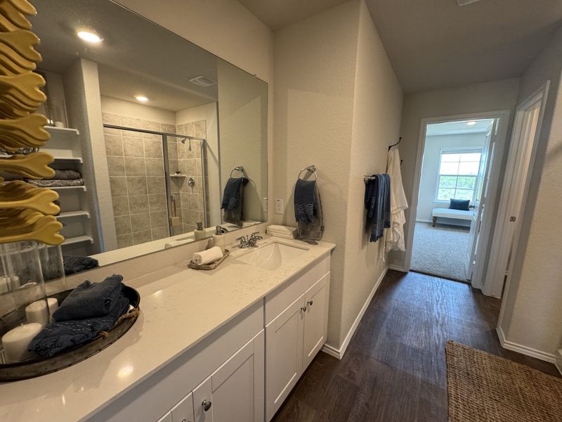 A modern bathroom features a sleek vanity, large mirror, and a tiled walk-in shower, leading to a bright bedroom.