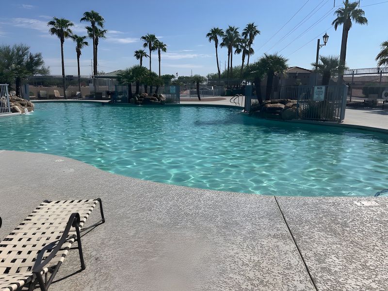 A serene pool with palm trees and lounge chairs at Magnolia at Desert Passage by KB Home in Maricopa, AZ.