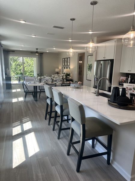 A modern kitchen and dining area with sleek countertops, pendant lighting, and large windows overlooking a lush view.