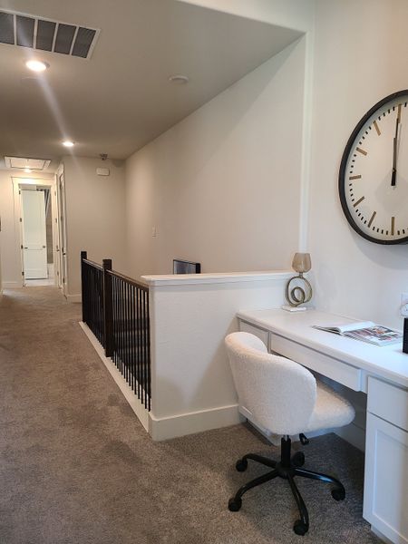 A cozy home office nook in a hallway, featuring a soft chair, sleek desk, large wall clock, and plush carpeting. A cozy home office nook in a hallway, featuring a soft chair, sleek desk, large wall clock, and plush carpeting.
