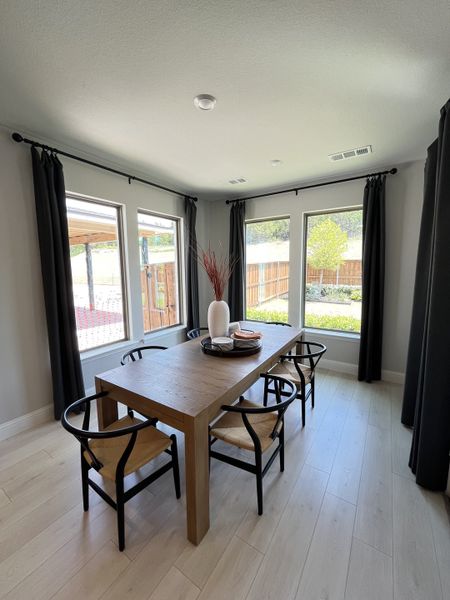 A chic dining area with a wooden table, stylish chairs, and floor-to-ceiling windows, creating a bright, inviting space.