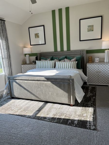 A modern bedroom with patterned bedding, green accent wall, and sleek decor, flooded with natural light.